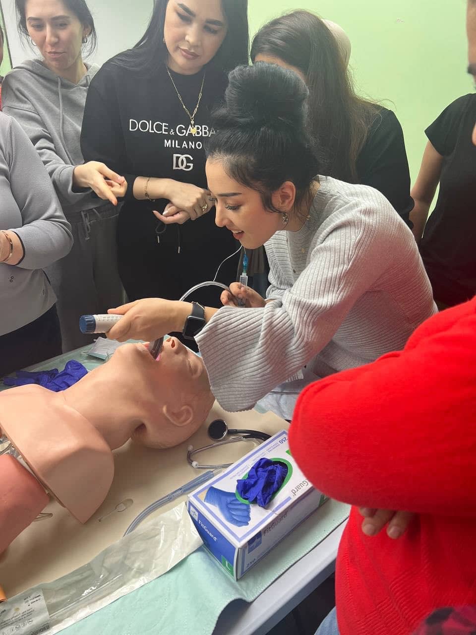A student practices an airway procedure on a training mannequin while classmates watch