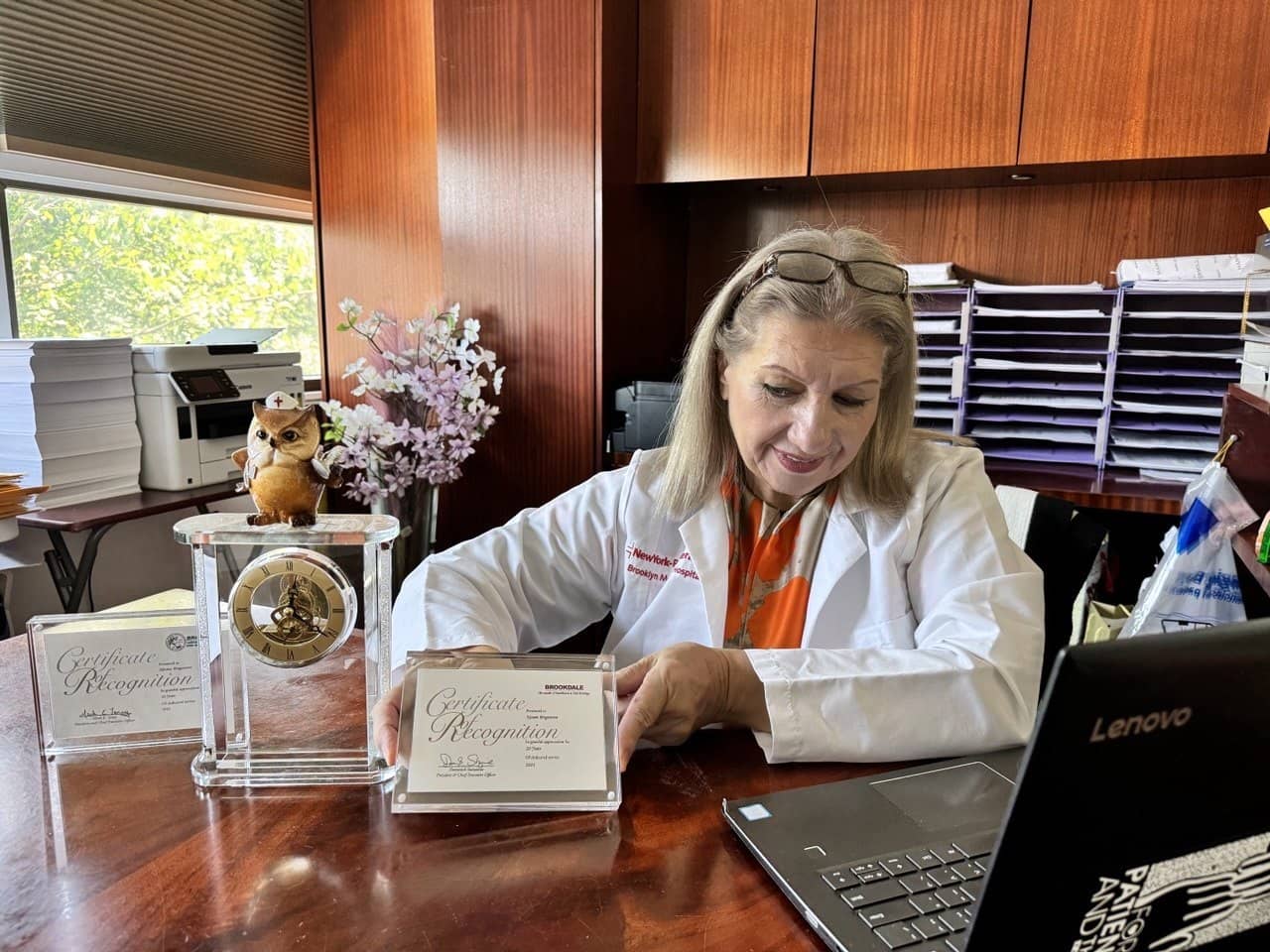 Ninara Ibragimova at her desk holding a certificate of recognition next to a laptop
