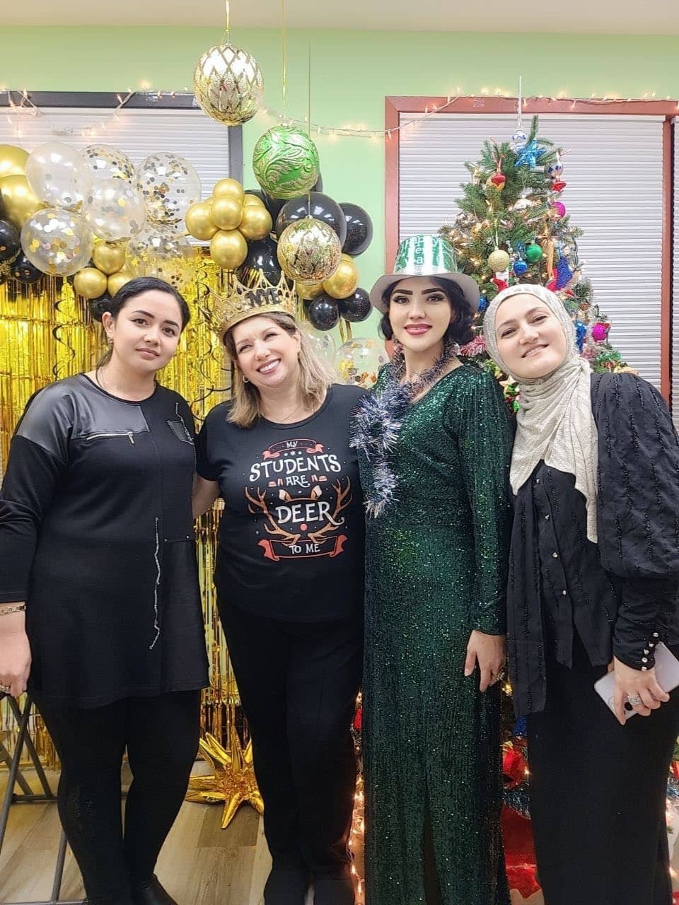 Four students in festive outfits by a decorated tree in the classroom