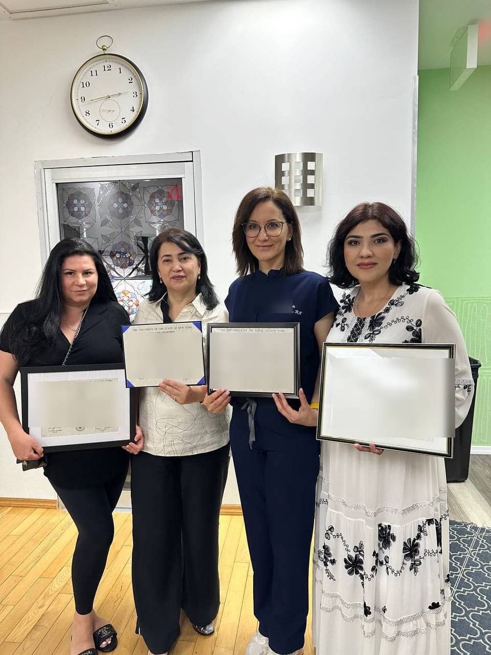 Четыре студентки в классе держат сертификаты Registered Professional Nurse штата Нью-Йорк в рамках